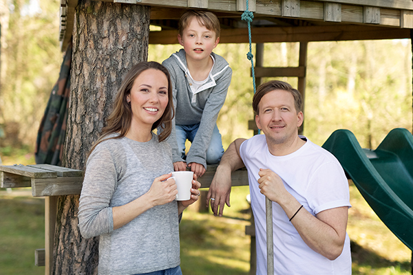 Familie med mor, far og ett barn foran en trehytt